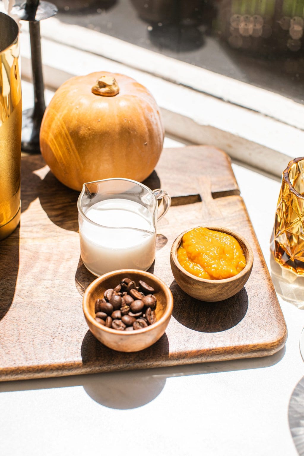 pumpkin creamer, coffee beans, and pumpkin puree on a cutting board with mini pumpkins as decor