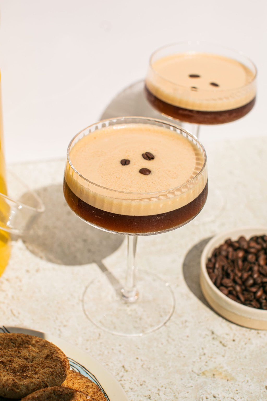 two glasses of espresso martinis with foam on top and three espresso beans for garnish