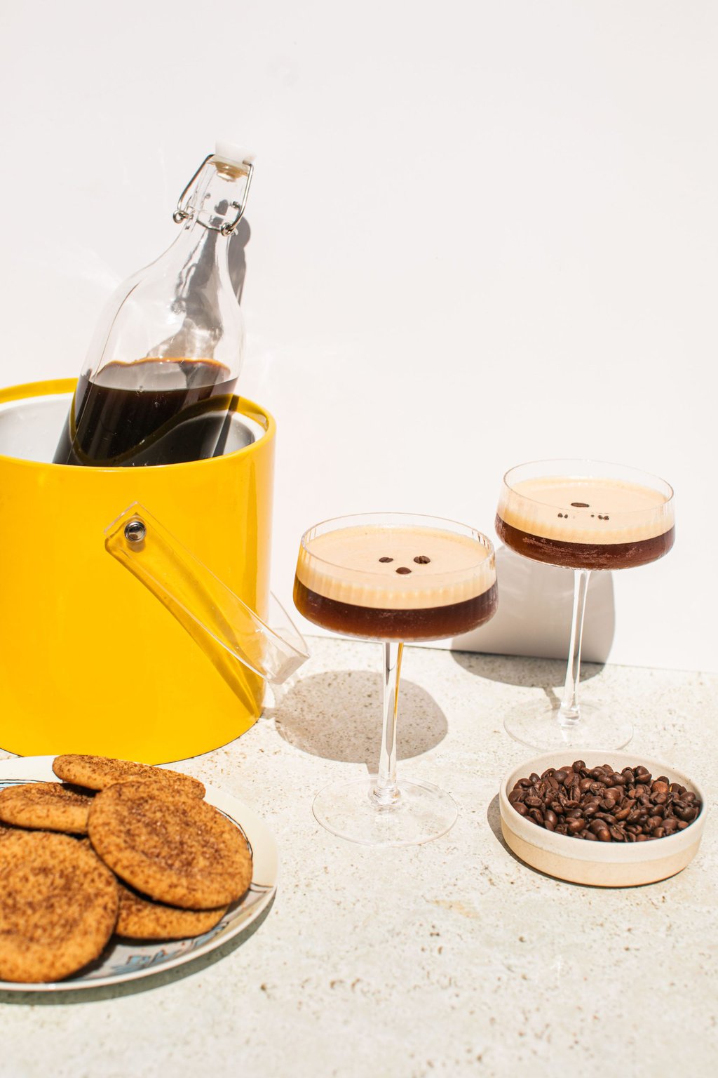 a large glass bottle in an ice bucket with two glasses of espresso martini beside it