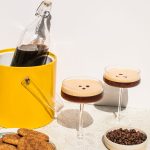 a bottle full of espresso martinis with two individual glasses to the side, alongside cookies and espresso beans