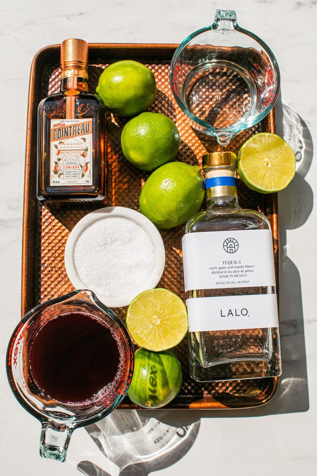 tequila, pomegranate juice, limes, salt, cointreau, and agave on a bronze tray