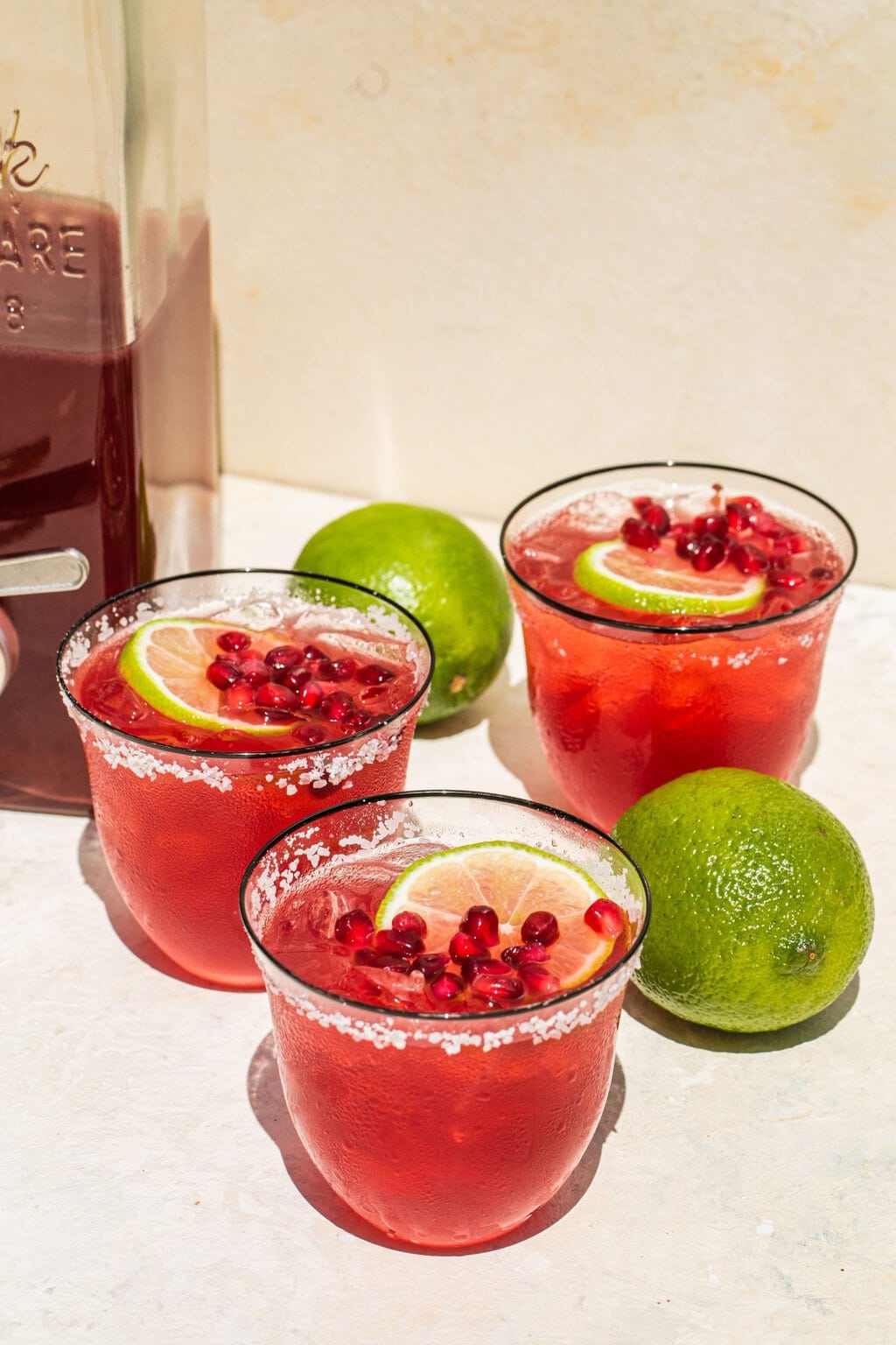 three glasses of pomegranate margaritas with salted rims and lime and pomegranate seed garnish