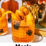 a maple old fashioned with donut garnish on top and syrup being poured over the donuts, also with text overlay at the bottom of the image