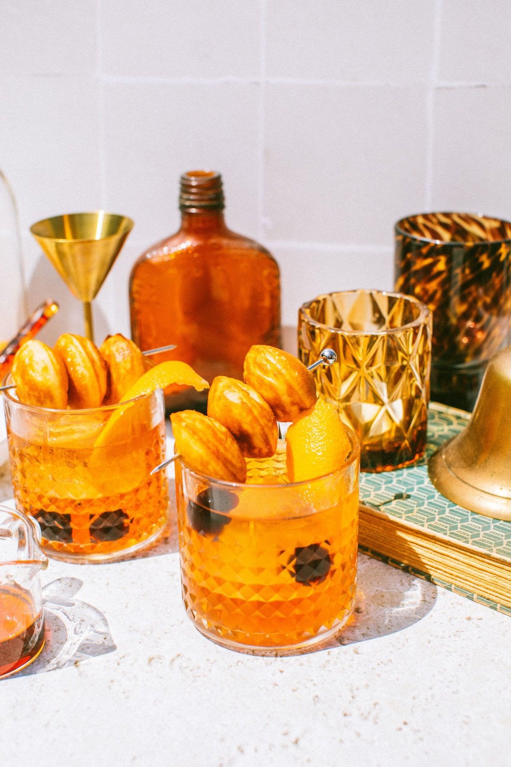 a couple glasses of maple old fashioned cocktails garnished with an orange peel and donut holes on a skewer