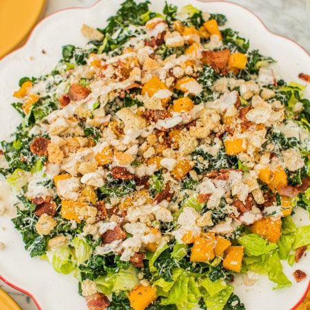 a large serving platter of kale caesar salad drizzled in homemade dressing