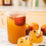 a big pitcher of bourbon apple cider with two glasses of the cocktail in front