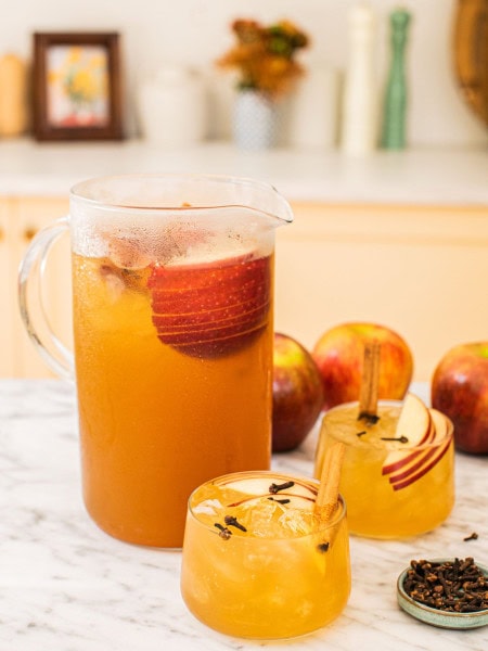 a big pitcher of bourbon apple cider with two glasses of the cocktail in front