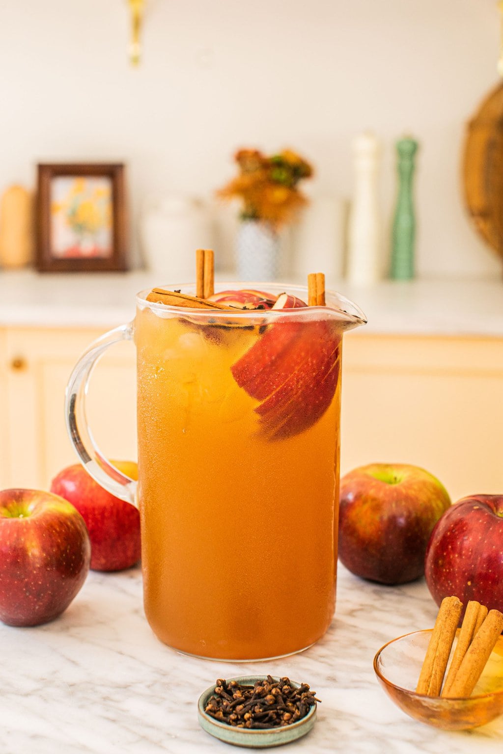 a large pitcher full of bourbon and apple cider with apples, cinnamon sticks, and star anise scattered around the surface beside it