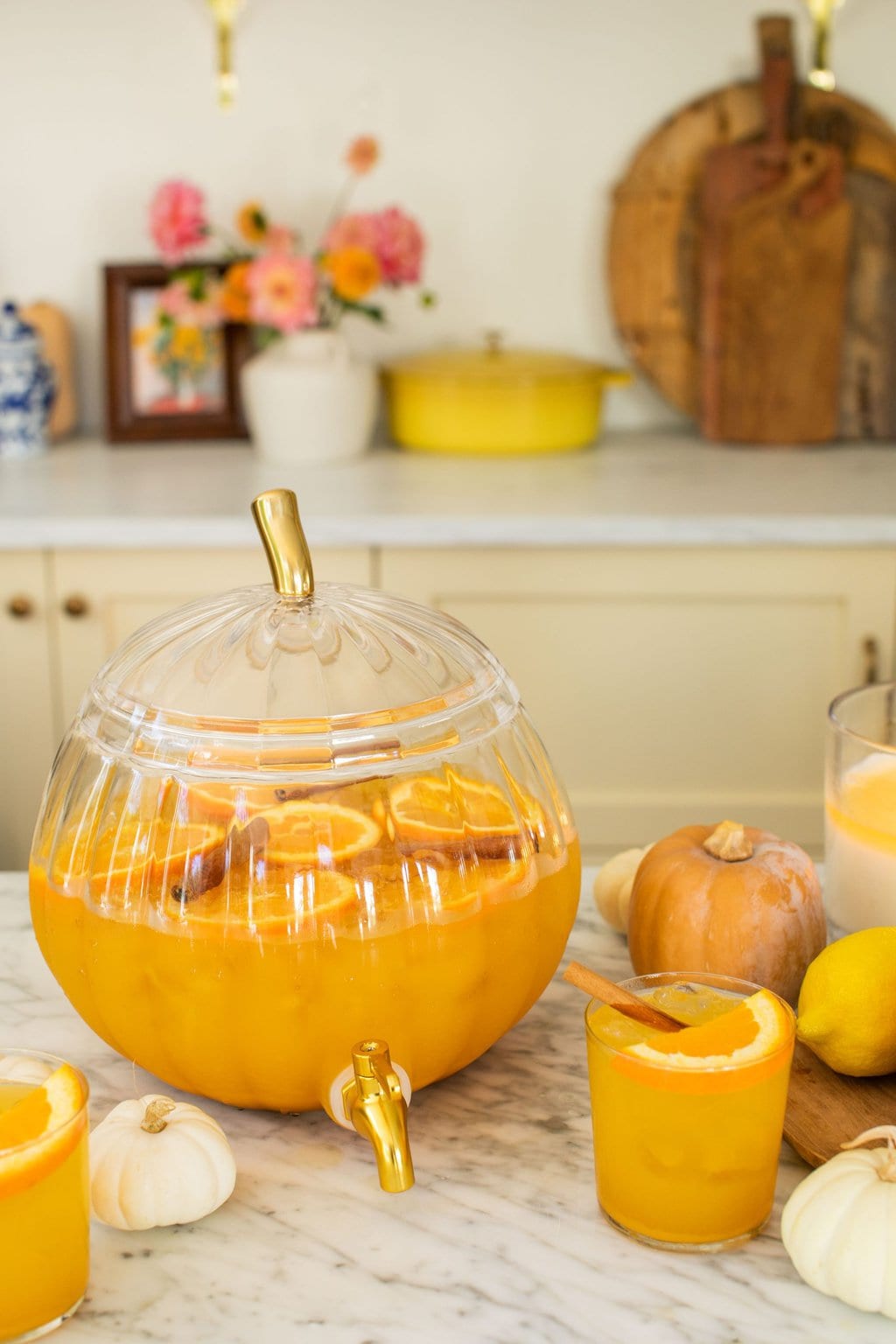 glass pumpkin full of punch with a glass in front of it and mini pumpkins scattered around