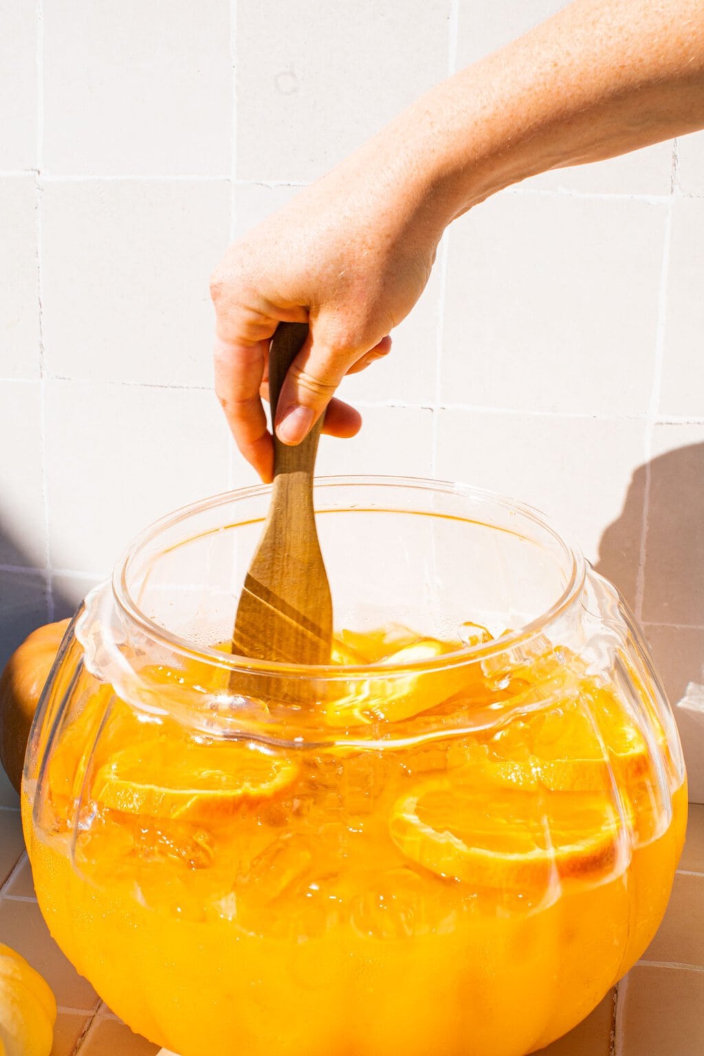 and hand stirring the punch with a wooden spoon in a large glass pumpkin pitcher