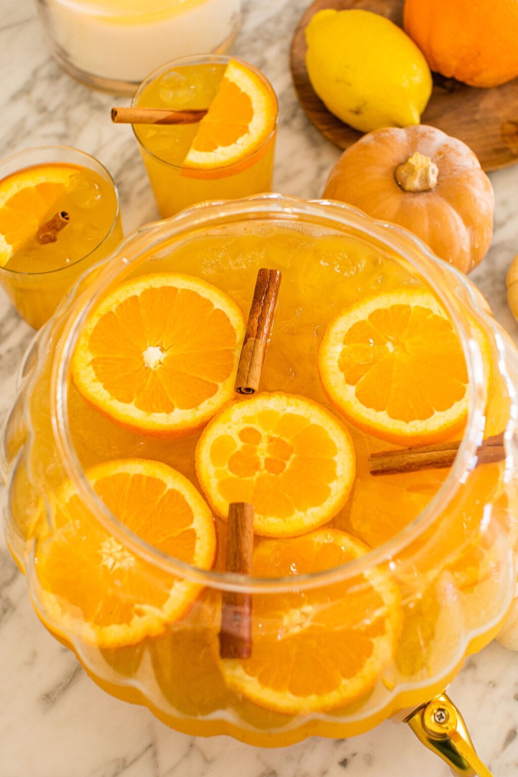 an overhead shot of the punch in a clear glass pumpkin pitcher garnished with orange slices and cinnamon sticks