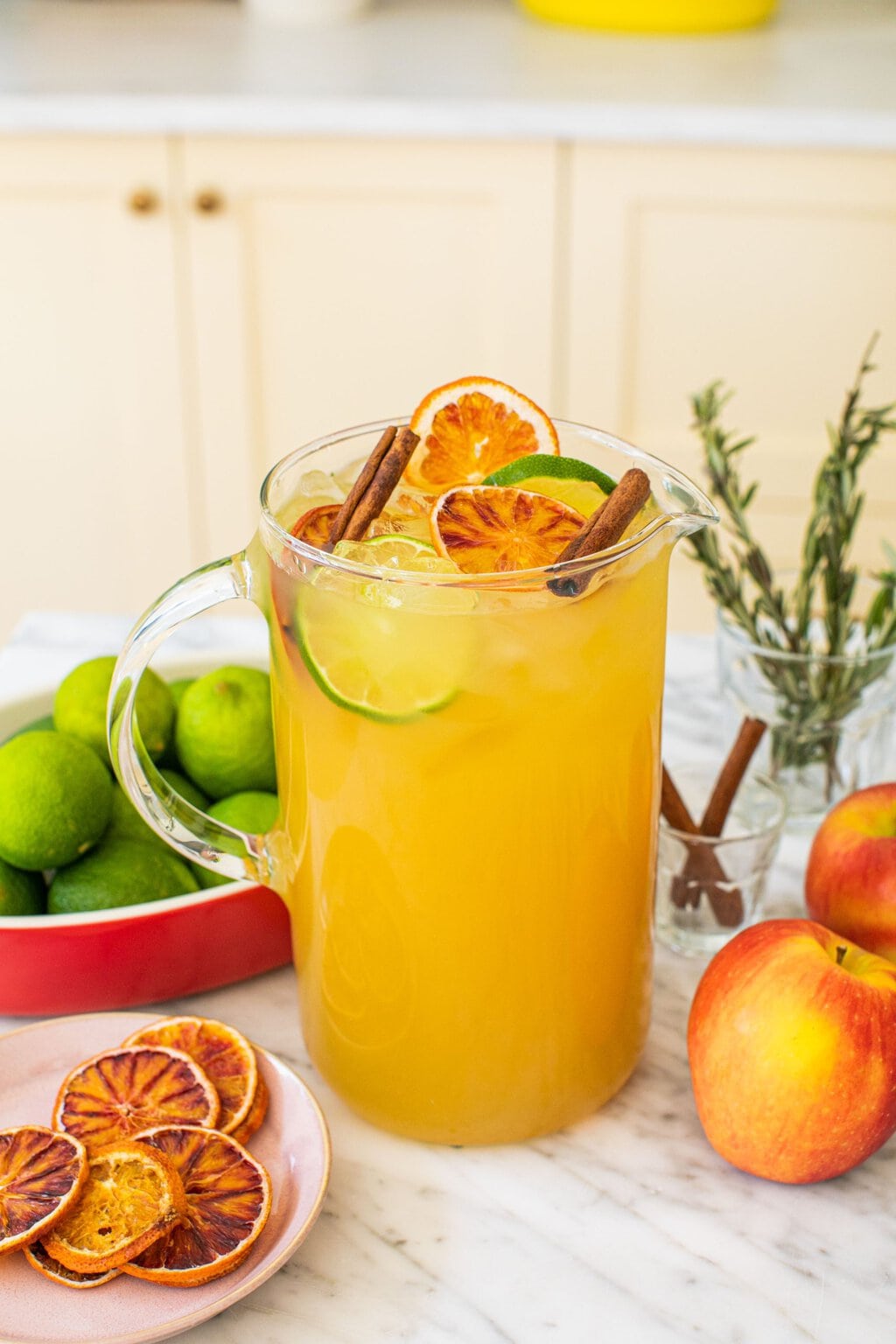 a large pitcher of cider margaritas with cinnamon sticks, lime slices, and dried oranges garnishing the top