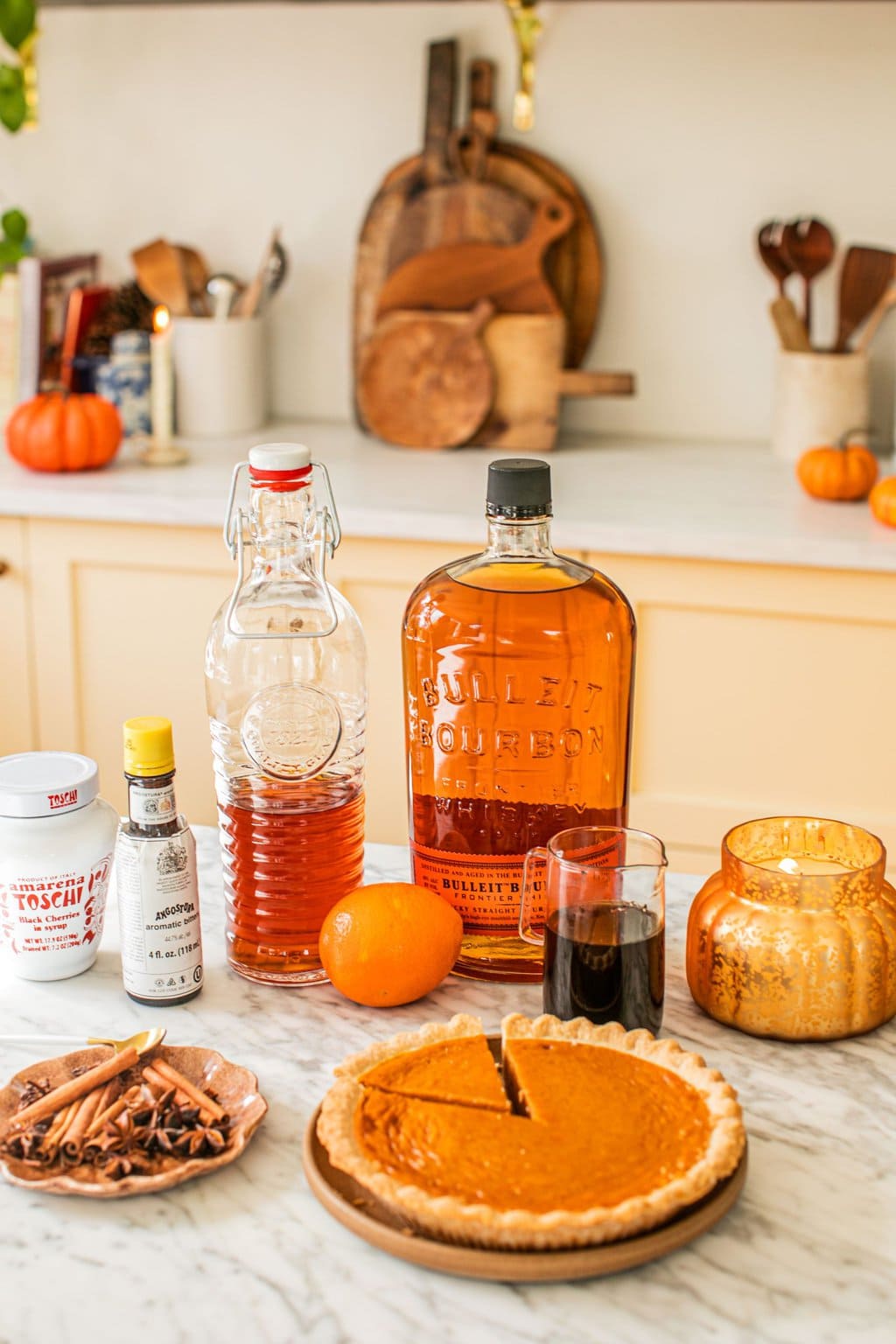 bourbon, simple syrup, aromatic bitters, oranges, a candle, cinnamon sticks, star anise, and a pumpkin pie