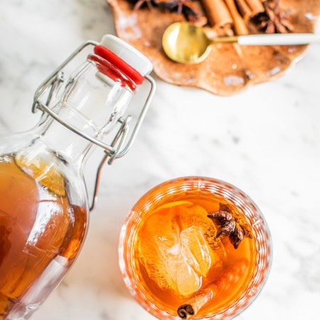 an old fashioned photographed from above with a swing top bottle hovering above and a small plate with garnish in the top right corner of the photo