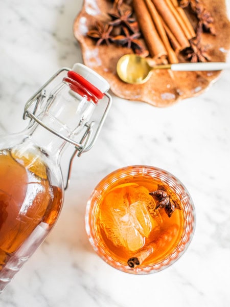 an old fashioned photographed from above with a swing top bottle hovering above and a small plate with garnish in the top right corner of the photo