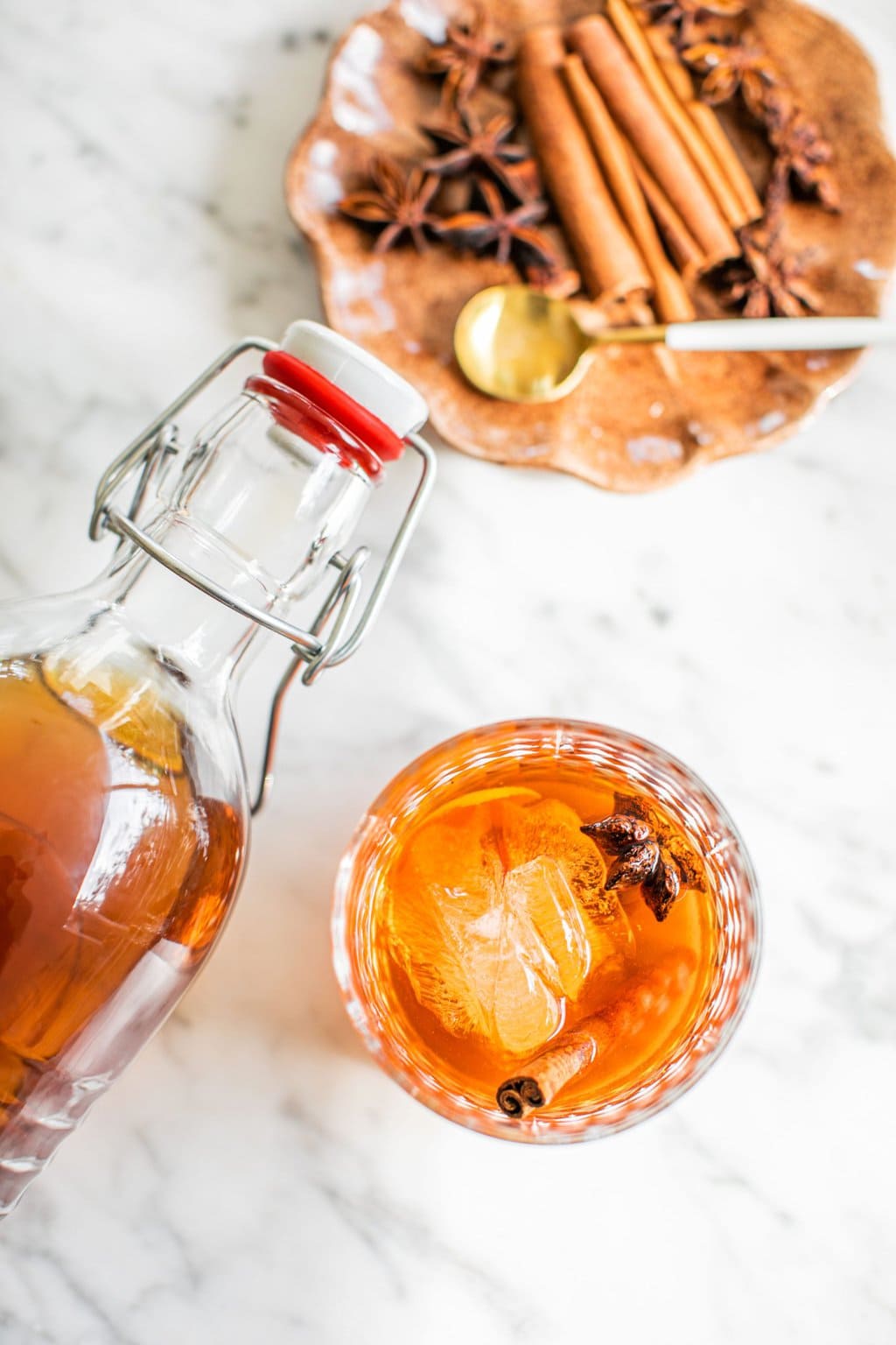 an old fashioned photographed from above with a swing top bottle hovering above and a small plate with garnish in the top right corner of the photo