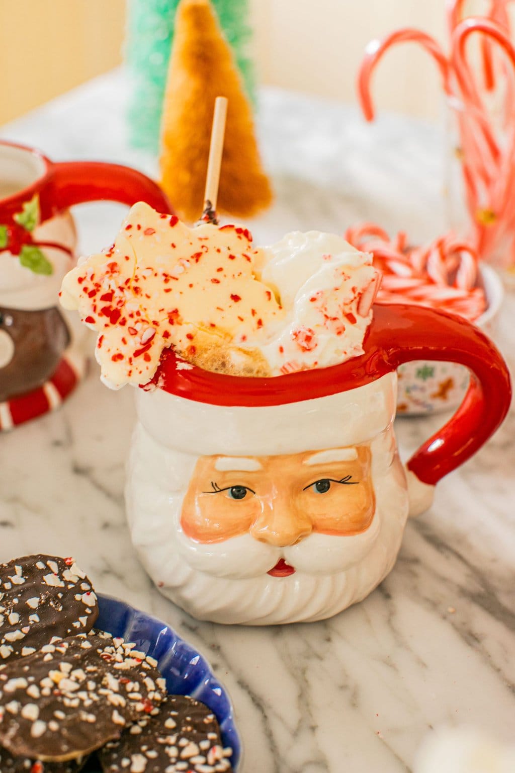 a santa mug full of hot chocolate and topped with whipped cream, and crushed peppermint