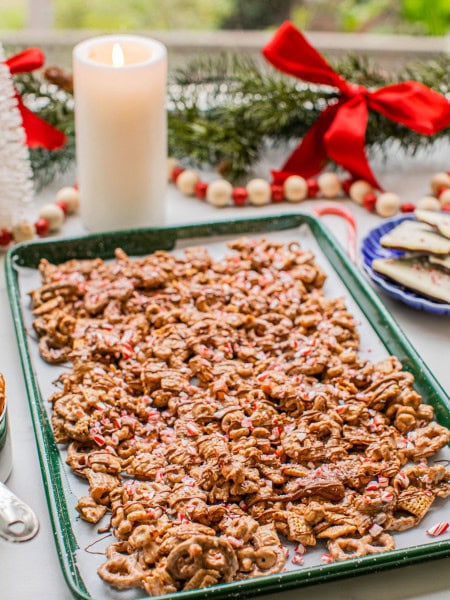 peppermint bark puppy chow on a baking sheet with christmas decor and a candle around it