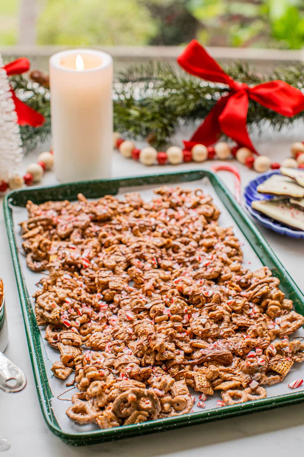 peppermint bark puppy chow on a baking sheet with christmas decor and a candle around it