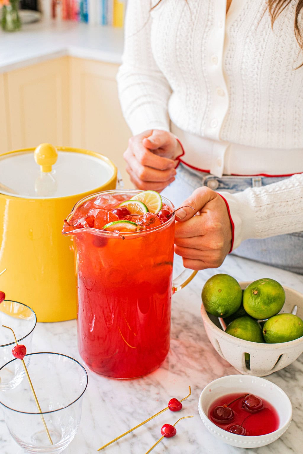 elizabeth holding a pitcher of dirty shirleys with an ice bucket, limes, and extra cherries on the side