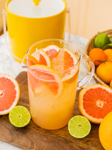 a large pitcher of grapefruit palomas with grapefruits and limes around it