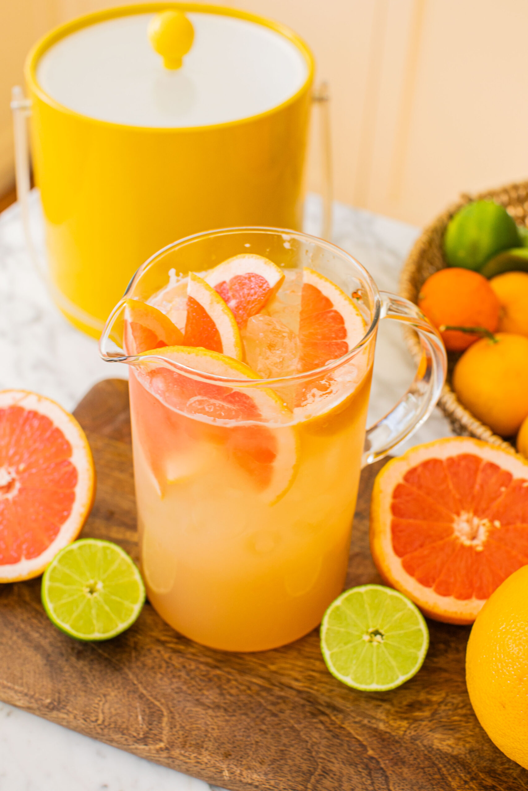 a large pitcher of grapefruit palomas with grapefruits and limes around it