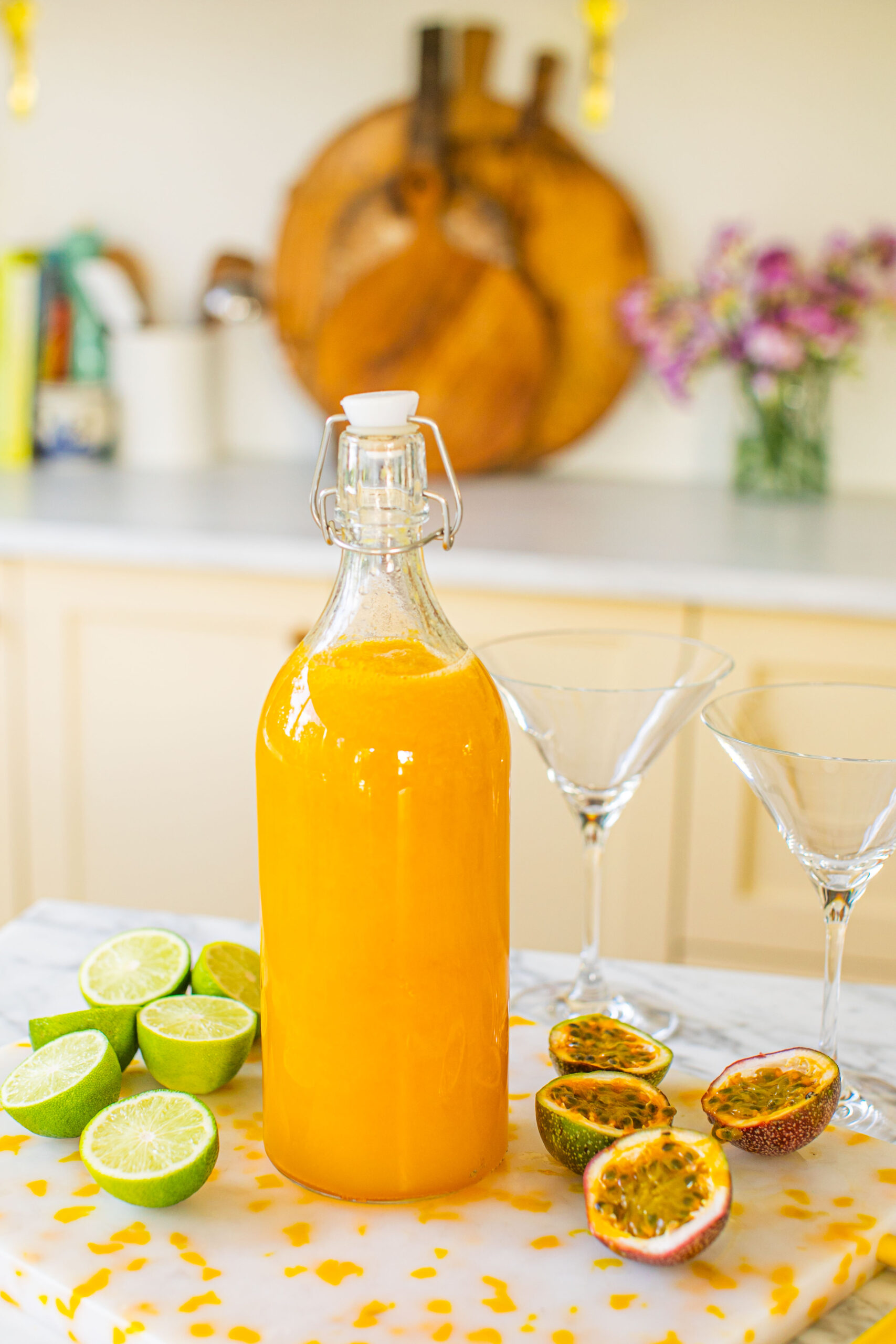 a large bottle of passion fruit martinis beside passion fruits, limes, and two martini glasses