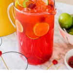 a large pitcher of dirty shirleys garnished with cherries and lime