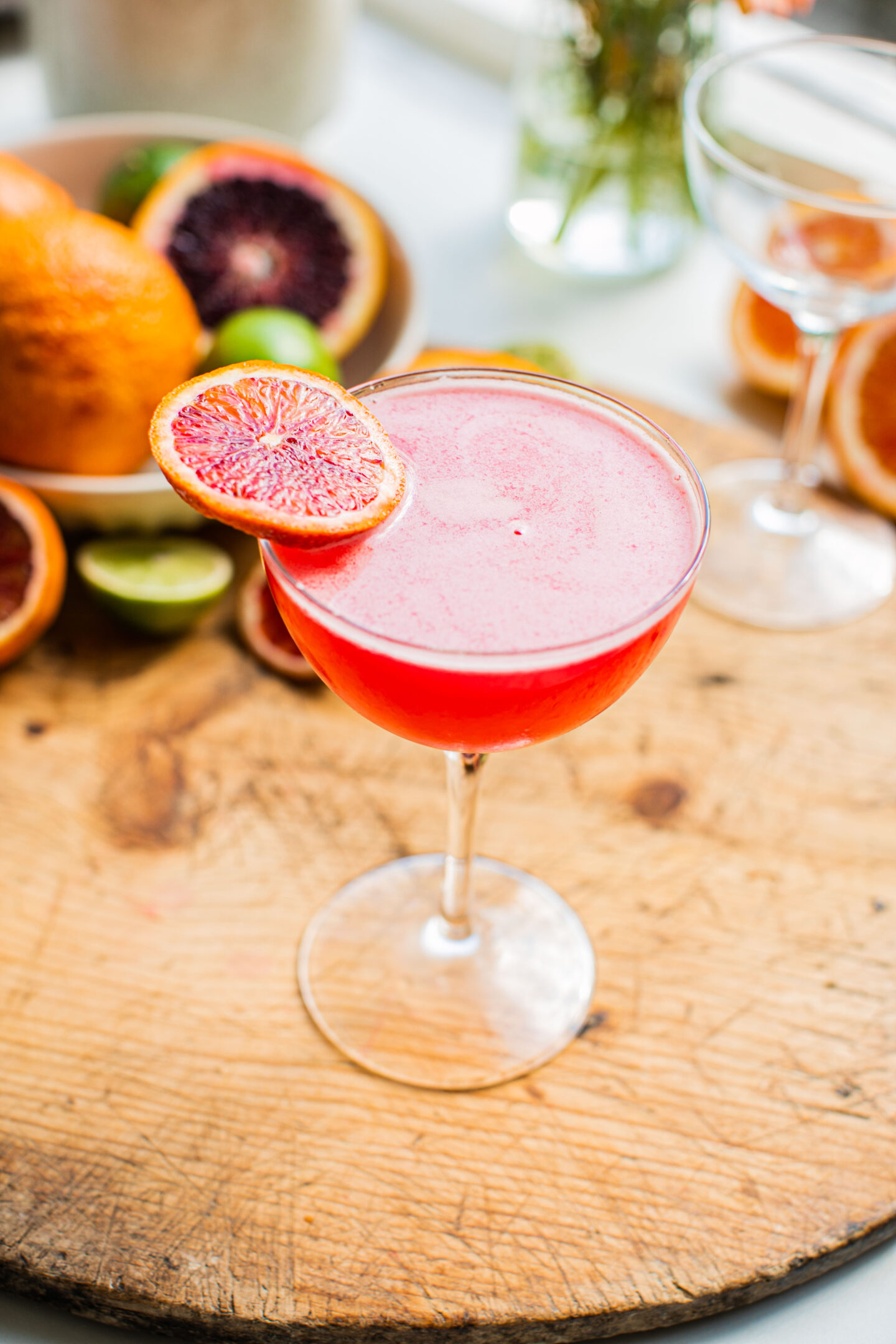 a blood orange martini on a wooden surface garnished with a blood orange wheel