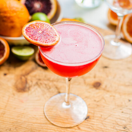 a blood orange martini on a wooden surface garnished with a blood orange wheel