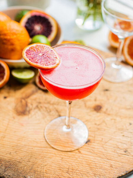 a blood orange martini on a wooden surface garnished with a blood orange wheel