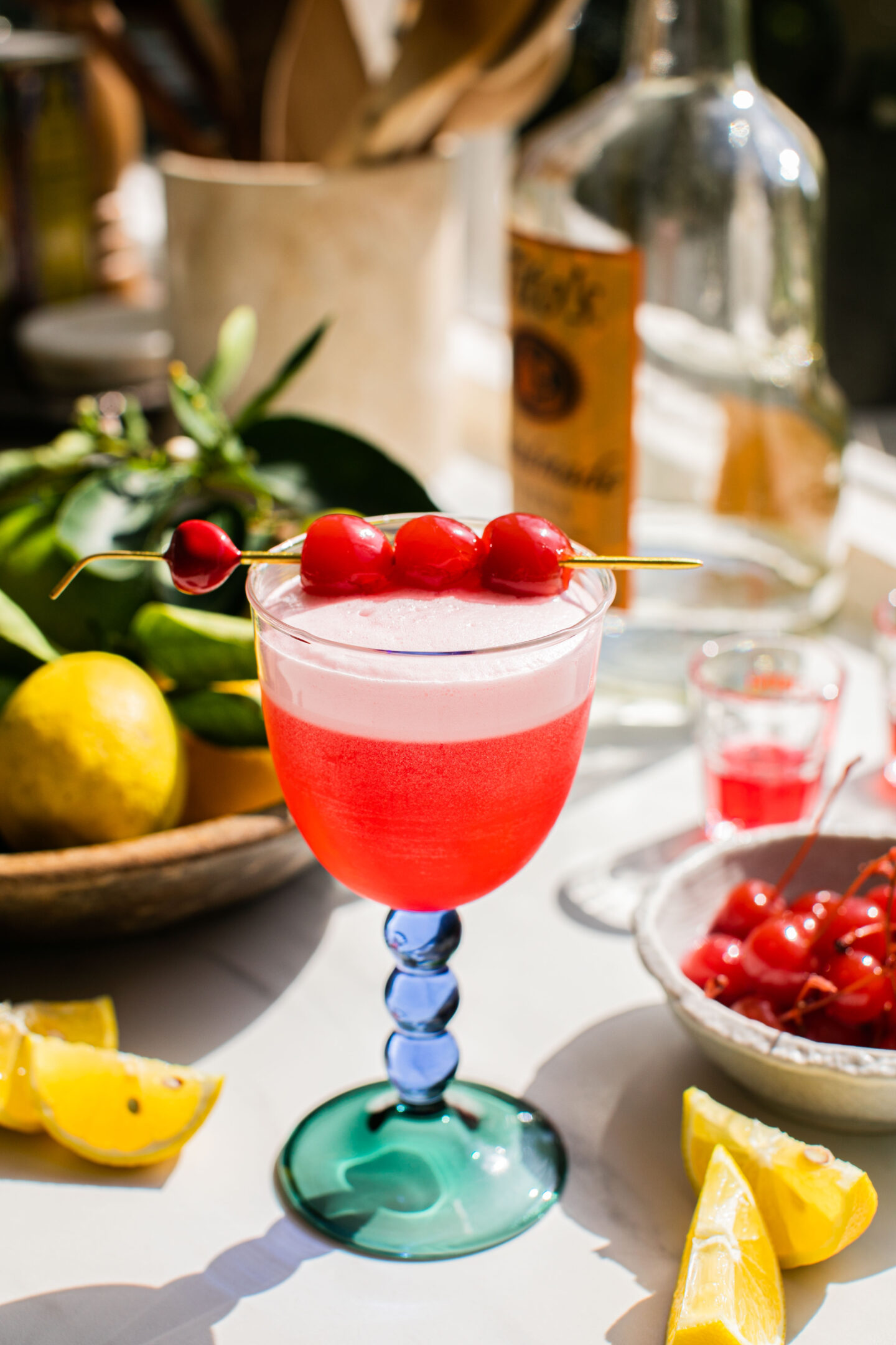 a glass of cherry vodka sour with vodka, cherries, and lemons in the background