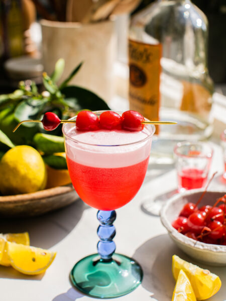 a glass of cherry vodka sour with vodka, cherries, and lemons in the background