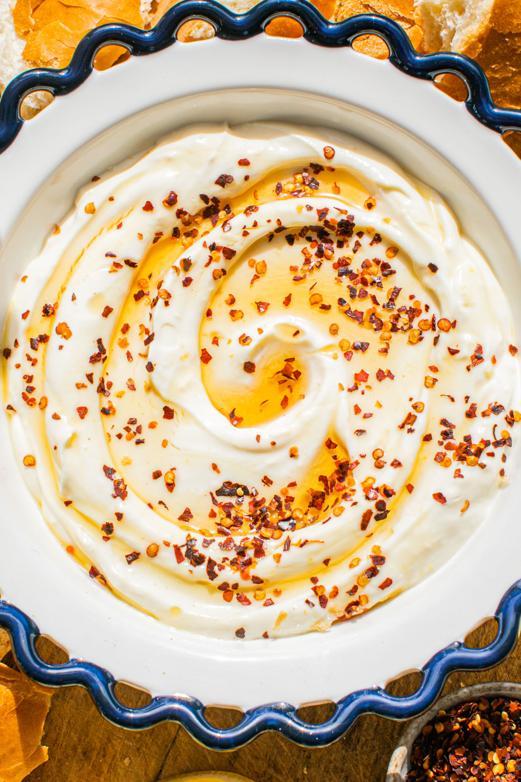 a closeup overhead photo of whipped ricotta in a bowl with hot honey drizzled on top and red pepper flakes sprinkled over it