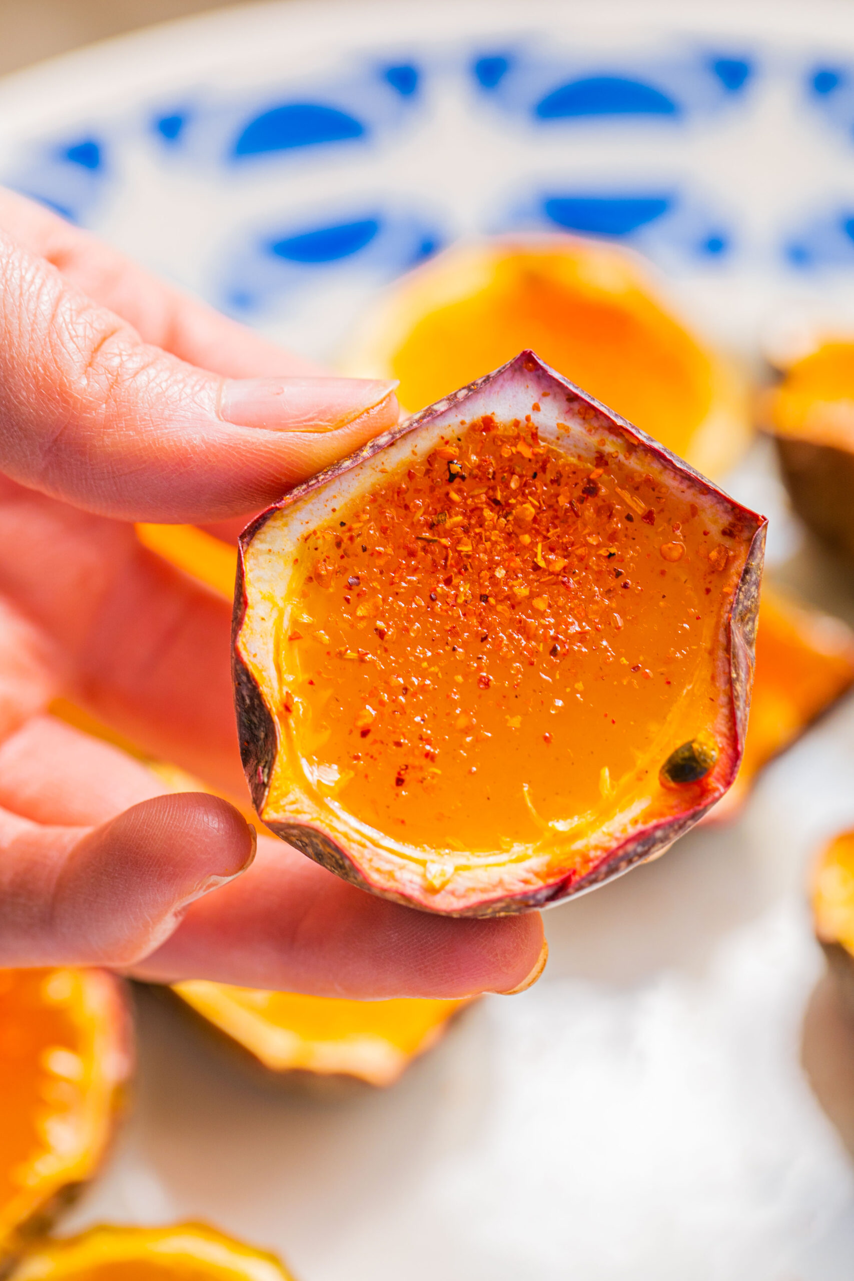 a hand holding a passion fruit half filled with a jello shot and garnished with tajin