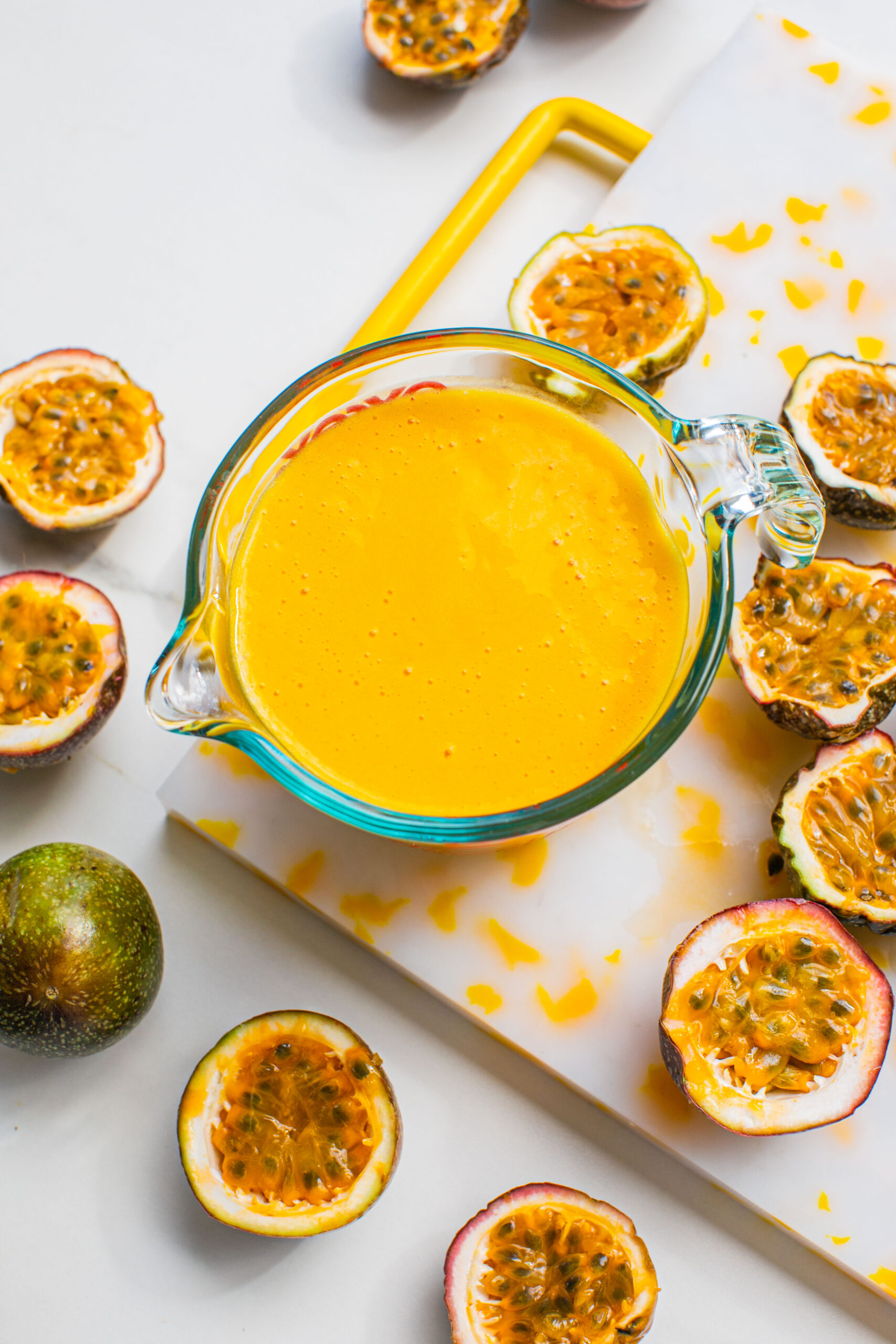 an overhead shot of passion fruit puree juice in a pyrex measuring glass with halved passionfruit scattered around