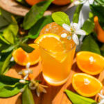 a glass of an orange gin and tonic with an orange blossom and orange slice as garnish, plus leaves and extra orange slices scattered around