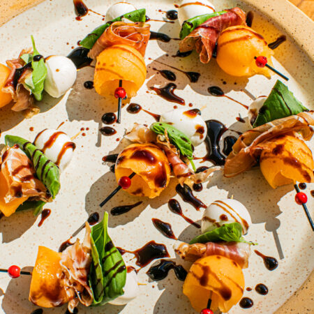 a plate with melon skewers displayed on it and balsamic glaze drizzled on top