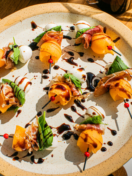 a plate with melon skewers displayed on it and balsamic glaze drizzled on top