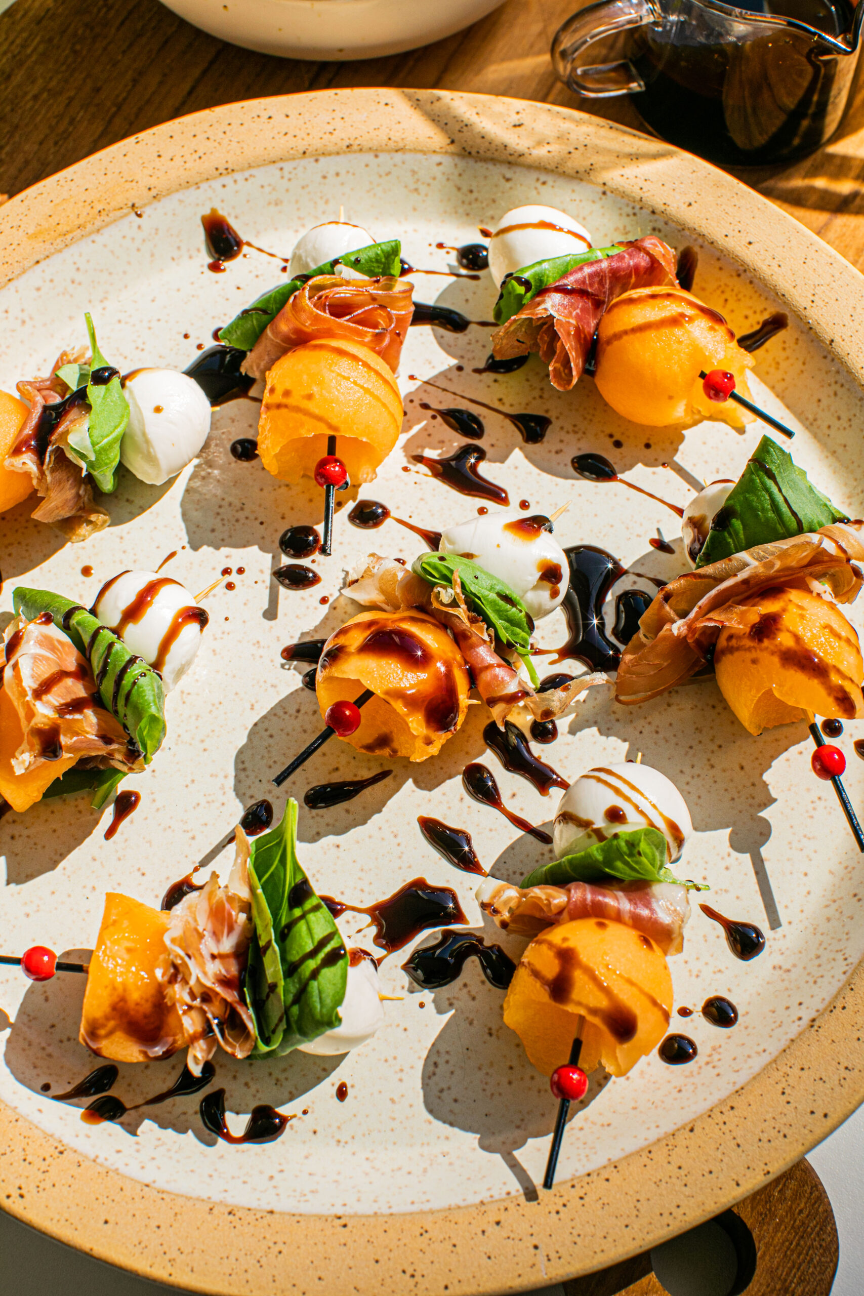 a plate with melon skewers displayed on it and balsamic glaze drizzled on top