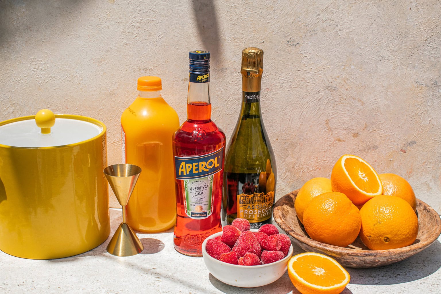 frozen raspberries, aperol, orange juice, prosecco, oranges, and an ice bucket