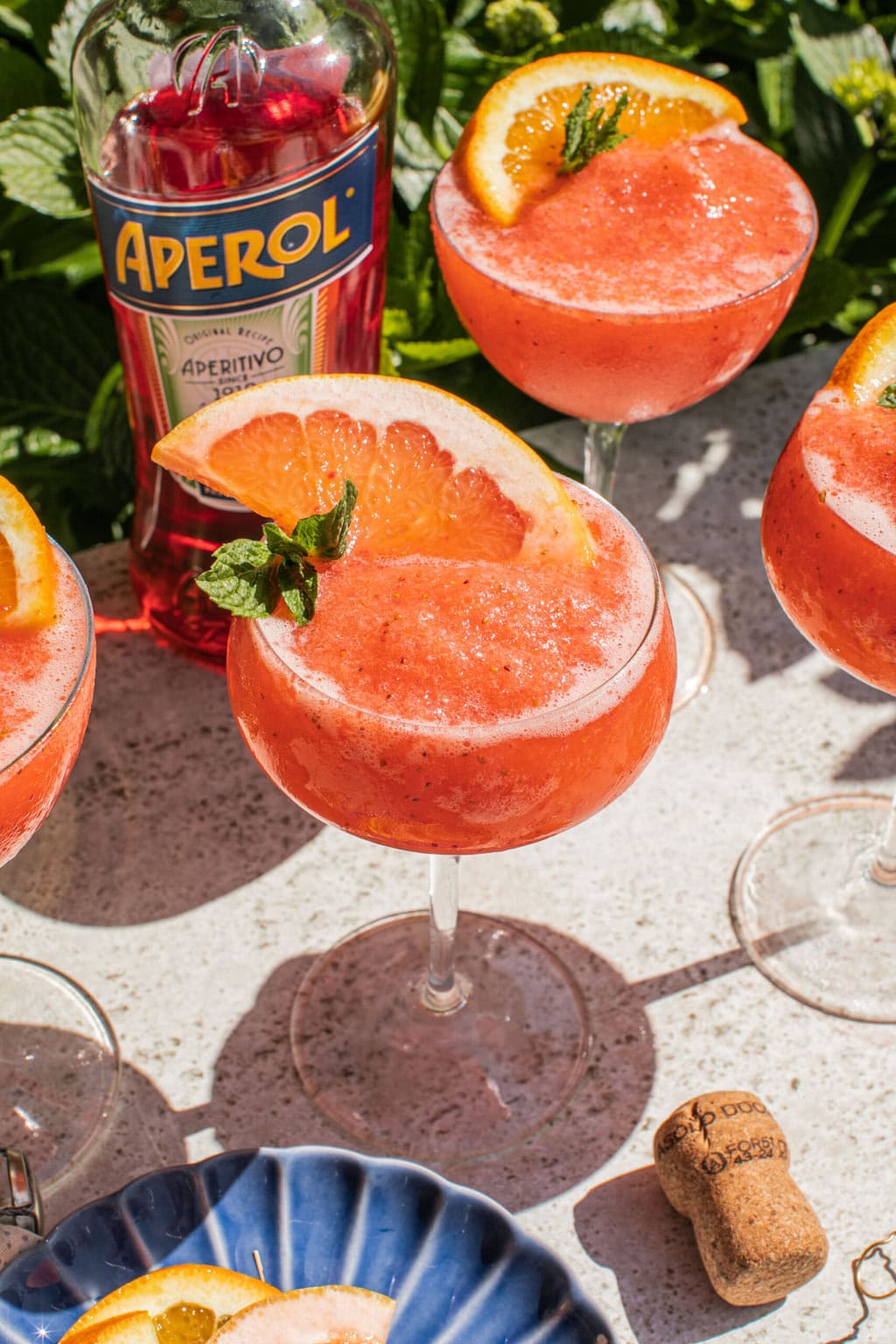 a bottle of aperol behind a few glasses of frozen aperol spritz