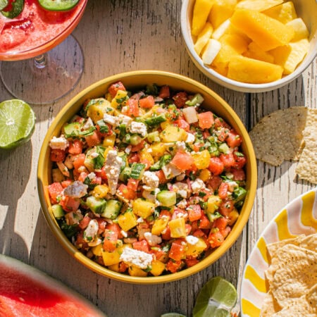 a large bowl of watermelon feta salsa with a watermelon cocktail and chips beside it