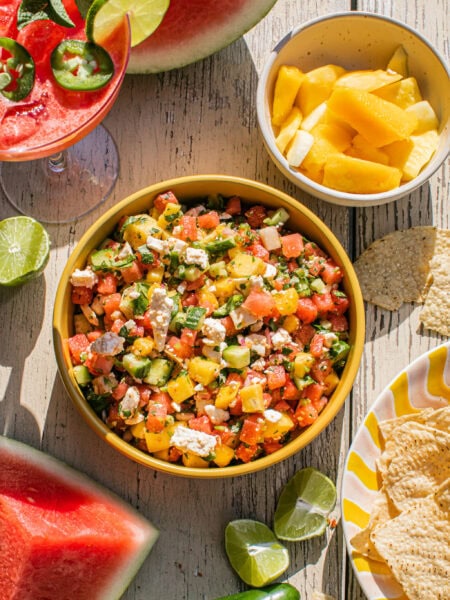 a large bowl of watermelon feta salsa with a watermelon cocktail and chips beside it