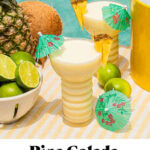 a mocktail pina colada with a tiny umbrella, limes, coconut, and pineapple