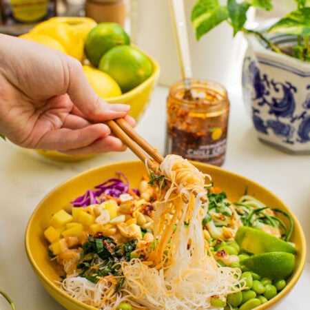 a bowl of spring roll ingredients that someone is taking a bite out of with chopsticks