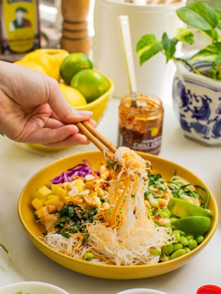 a bowl of spring roll ingredients that someone is taking a bite out of with chopsticks