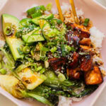 a bowl full of teriyaki salmon, cucumber, baby bok choy, avocado, and rice