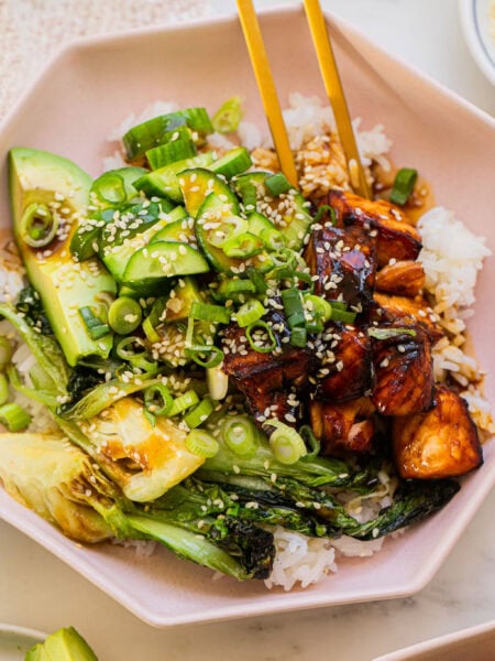 a bowl full of teriyaki salmon, cucumber, baby bok choy, avocado, and rice