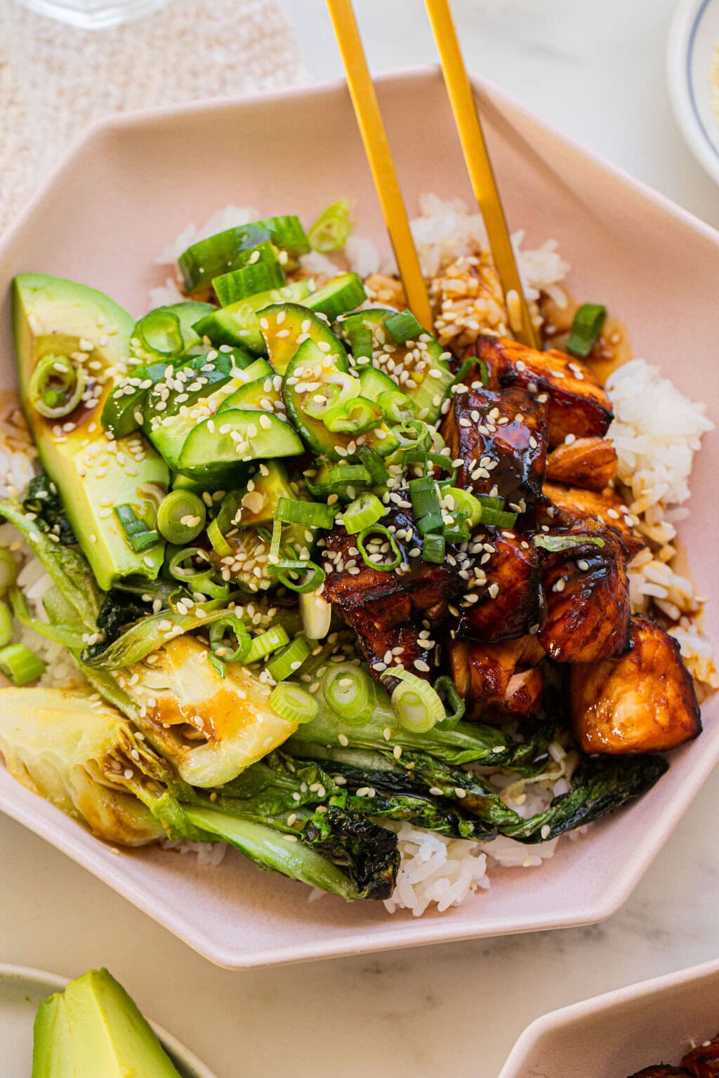 a bowl full of teriyaki salmon, cucumber, baby bok choy, avocado, and rice